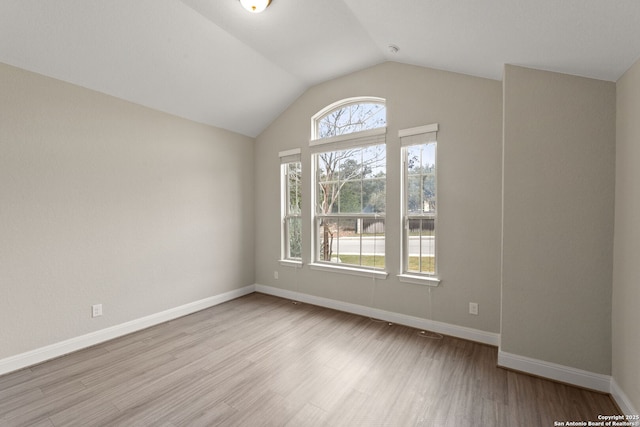 unfurnished room featuring lofted ceiling, a wealth of natural light, and light wood-type flooring