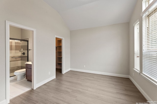 unfurnished bedroom with lofted ceiling, ensuite bathroom, light hardwood / wood-style floors, a walk in closet, and a closet