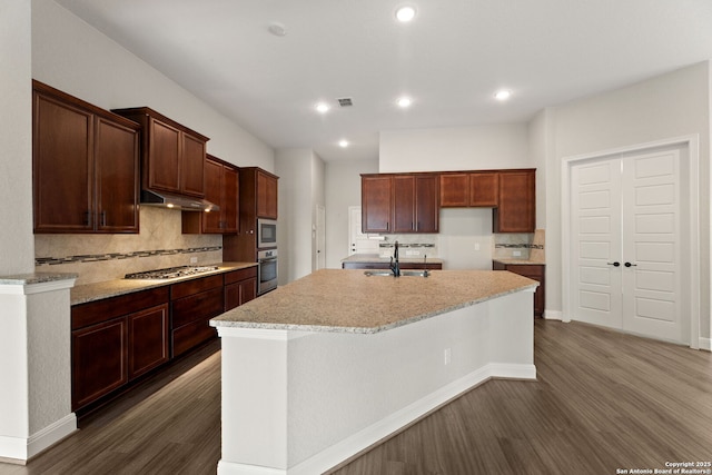 kitchen with dark hardwood / wood-style floors, tasteful backsplash, sink, stainless steel appliances, and a center island with sink