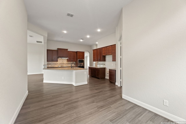 kitchen with dark hardwood / wood-style flooring, backsplash, and a center island with sink