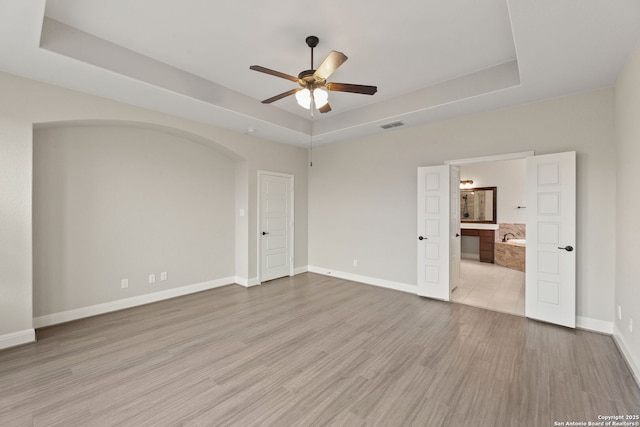 empty room featuring ceiling fan, a raised ceiling, and light hardwood / wood-style floors