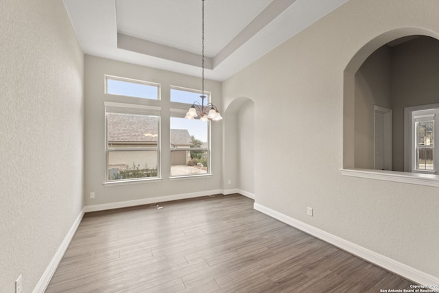 unfurnished dining area featuring wood-type flooring, a tray ceiling, and a notable chandelier