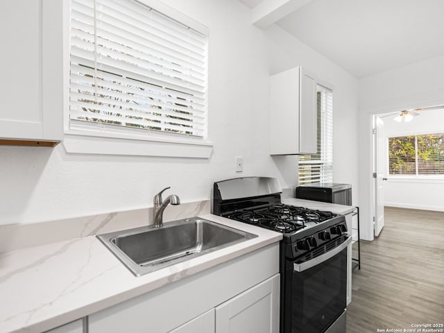 kitchen with sink, light stone counters, ceiling fan, gas range oven, and white cabinets