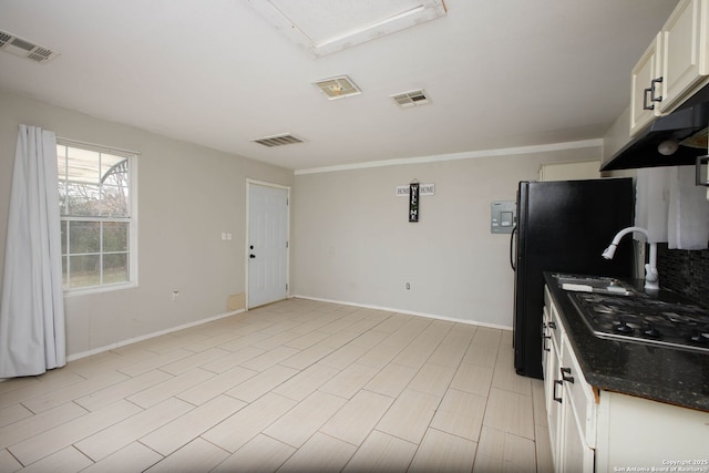 kitchen featuring sink, white cabinetry, black fridge, stainless steel gas stovetop, and dark stone counters