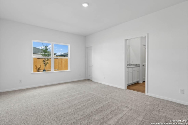 unfurnished bedroom featuring light colored carpet, connected bathroom, and sink