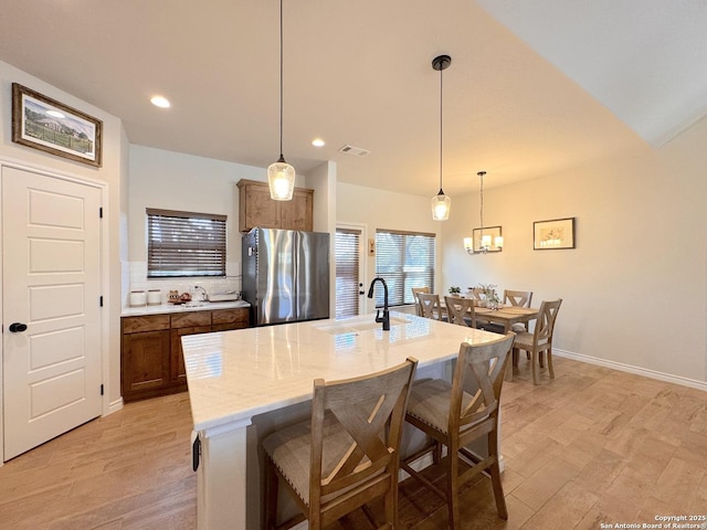 kitchen with light hardwood / wood-style flooring, stainless steel fridge, a kitchen breakfast bar, a center island with sink, and decorative light fixtures