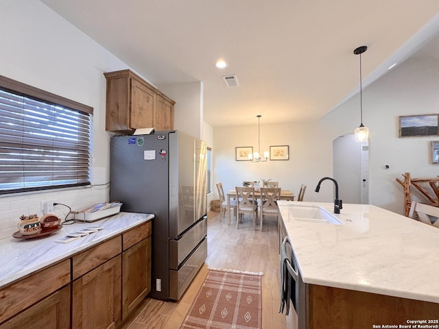 kitchen with hanging light fixtures, an island with sink, sink, and stainless steel refrigerator