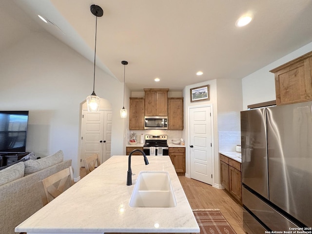 kitchen with sink, appliances with stainless steel finishes, hanging light fixtures, an island with sink, and decorative backsplash