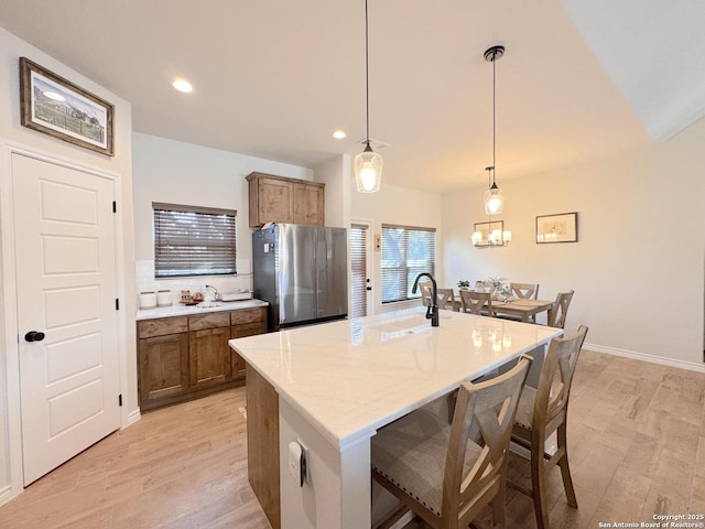 kitchen featuring decorative light fixtures, a kitchen breakfast bar, stainless steel fridge, an island with sink, and light hardwood / wood-style floors