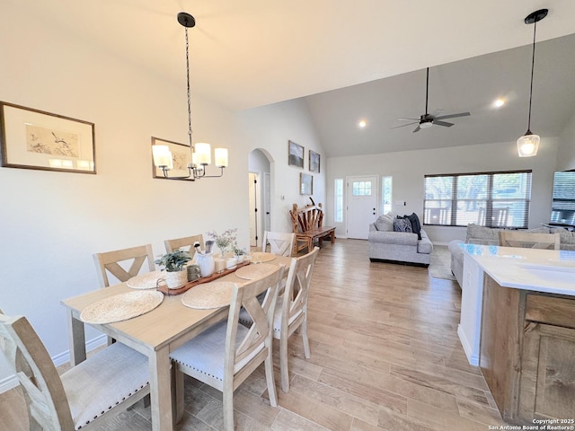 dining room featuring high vaulted ceiling, ceiling fan with notable chandelier, and light wood-type flooring