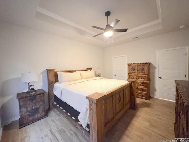 bedroom with ceiling fan, a raised ceiling, and light hardwood / wood-style flooring