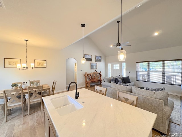 kitchen featuring lofted ceiling, sink, light hardwood / wood-style floors, a kitchen island with sink, and ceiling fan with notable chandelier