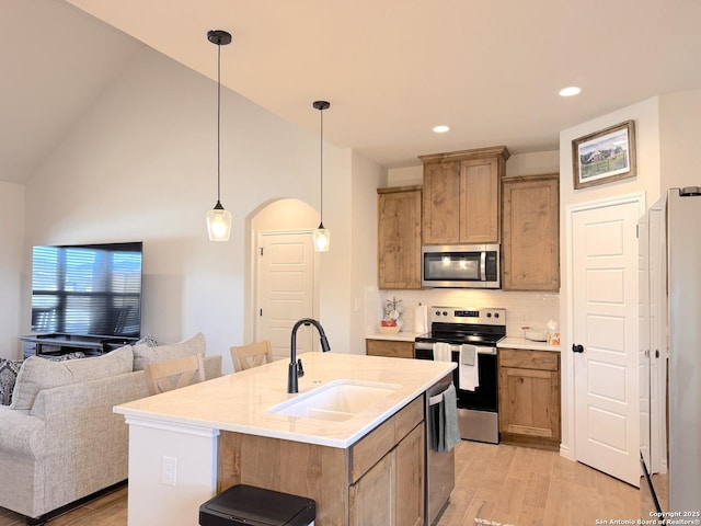 kitchen with decorative light fixtures, sink, backsplash, stainless steel appliances, and a center island with sink