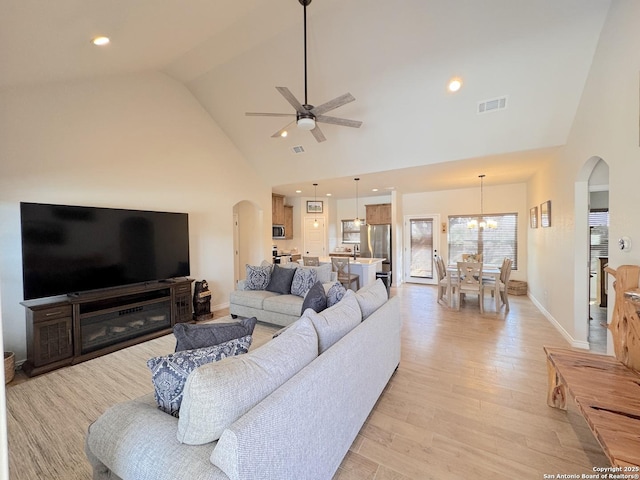 living room with high vaulted ceiling, ceiling fan with notable chandelier, and light hardwood / wood-style floors