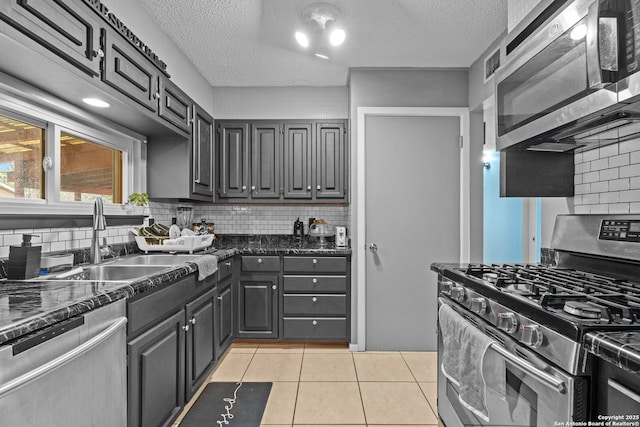 kitchen with sink, light tile patterned floors, appliances with stainless steel finishes, tasteful backsplash, and a textured ceiling