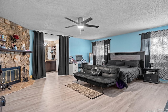 bedroom with connected bathroom, light hardwood / wood-style flooring, a textured ceiling, ceiling fan, and a fireplace