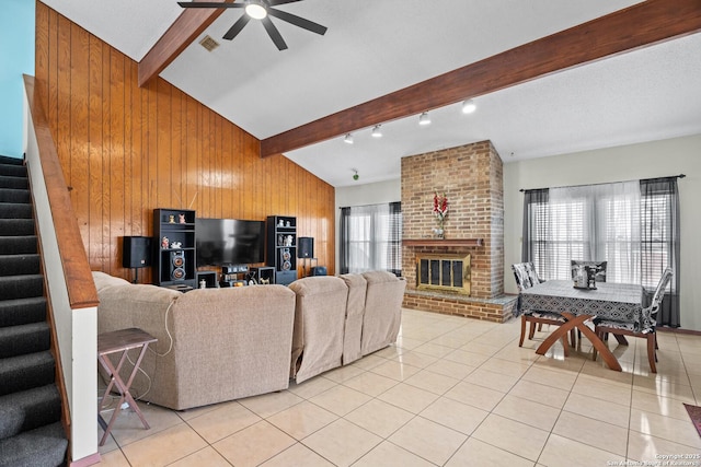 living room with ceiling fan, vaulted ceiling with beams, a fireplace, light tile patterned flooring, and wood walls