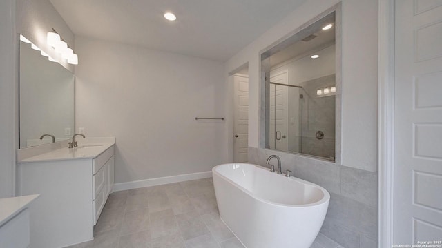 full bathroom featuring a stall shower, vanity, a freestanding tub, recessed lighting, and baseboards