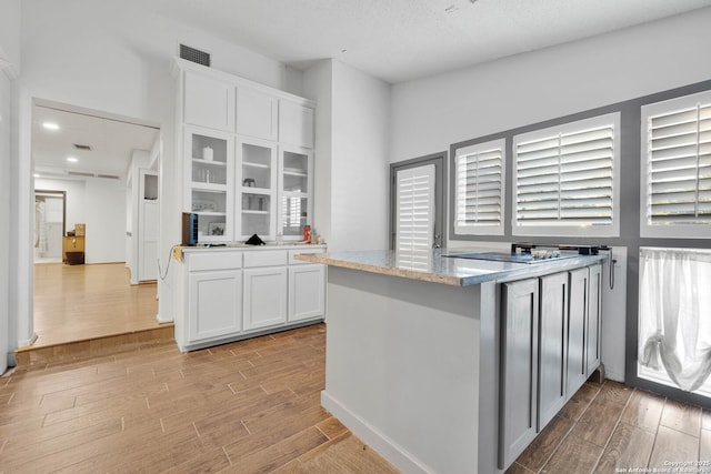 kitchen with white cabinetry, light stone counters, kitchen peninsula, and a textured ceiling