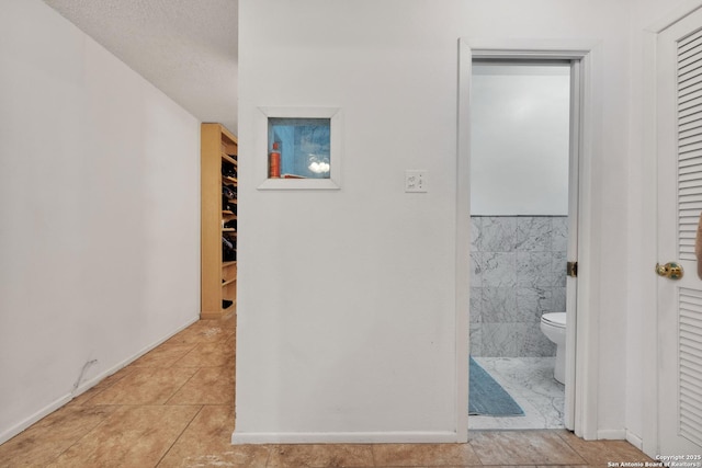 hallway with light tile patterned flooring, tile walls, and a textured ceiling