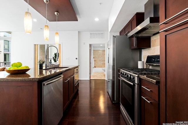 kitchen featuring sink, dark stone counters, hanging light fixtures, stainless steel appliances, and wall chimney exhaust hood