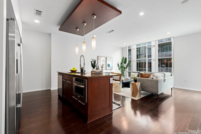 kitchen featuring a breakfast bar, sink, hanging light fixtures, stainless steel appliances, and a center island with sink