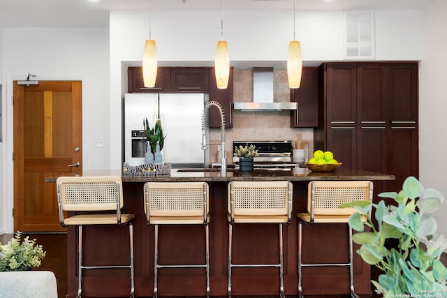 kitchen featuring wall chimney exhaust hood, a breakfast bar area, range, stainless steel fridge with ice dispenser, and pendant lighting