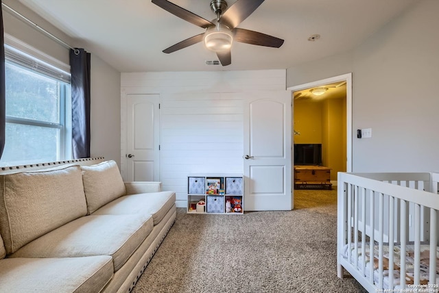 bedroom featuring a nursery area, ceiling fan, and carpet flooring