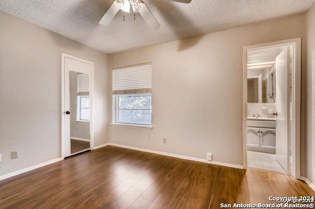 unfurnished bedroom featuring ceiling fan, connected bathroom, dark hardwood / wood-style floors, and a textured ceiling