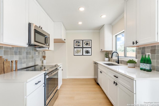 kitchen featuring sink, white cabinetry, ornamental molding, appliances with stainless steel finishes, and light hardwood / wood-style floors