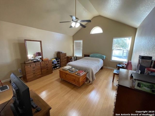 bedroom with ceiling fan, lofted ceiling, a textured ceiling, and light wood-type flooring