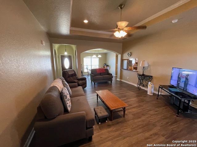 living room featuring ceiling fan, a raised ceiling, crown molding, dark wood-type flooring, and a textured ceiling