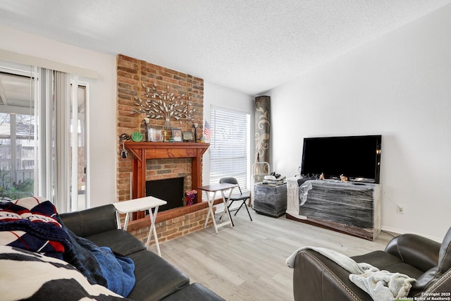 living room with a brick fireplace, a textured ceiling, and light wood-type flooring