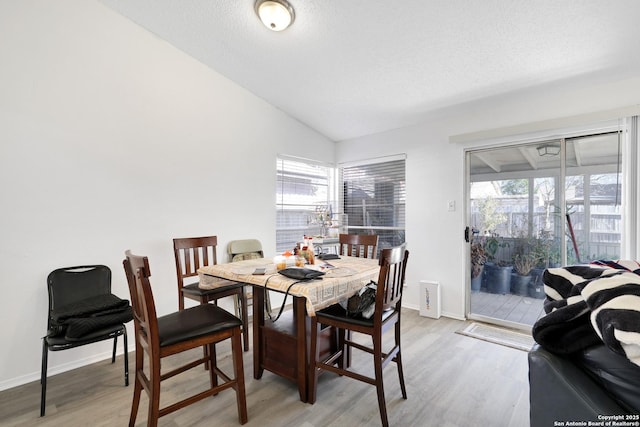 dining area with lofted ceiling, light hardwood / wood-style floors, and a textured ceiling