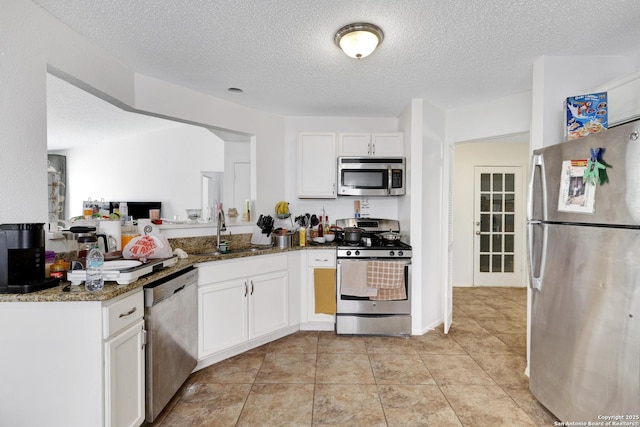 kitchen featuring sink, white cabinetry, dark stone countertops, stainless steel appliances, and a textured ceiling