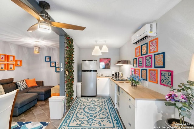 kitchen featuring light tile patterned floors, stainless steel refrigerator, ceiling fan, white cabinetry, and a wall mounted air conditioner