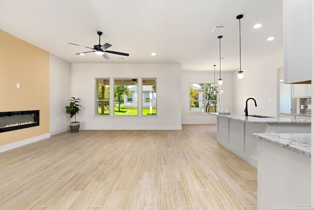 unfurnished living room featuring ceiling fan with notable chandelier, light hardwood / wood-style floors, and sink