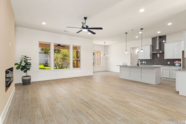 kitchen featuring pendant lighting, white cabinetry, decorative backsplash, light stone counters, and wall chimney exhaust hood