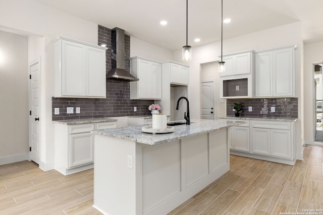 kitchen with sink, hanging light fixtures, white cabinets, a center island with sink, and wall chimney exhaust hood