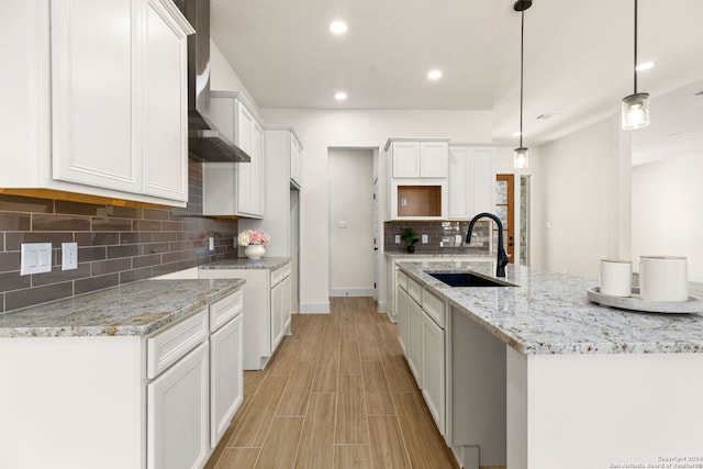 kitchen featuring sink, white cabinetry, a center island with sink, pendant lighting, and light stone countertops