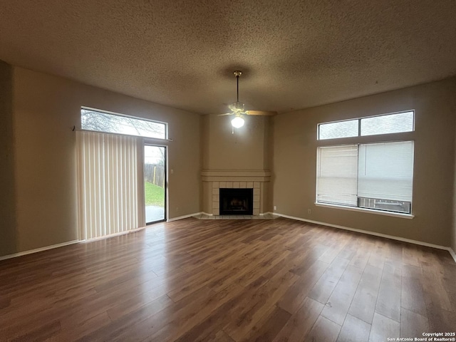 unfurnished living room featuring a tiled fireplace, ceiling fan, wood-type flooring, and a textured ceiling