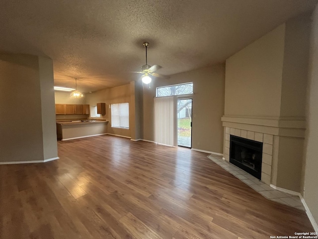 unfurnished living room with ceiling fan, a fireplace, a textured ceiling, and light wood-type flooring