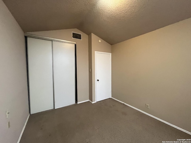 unfurnished bedroom featuring lofted ceiling, dark carpet, a closet, and a textured ceiling