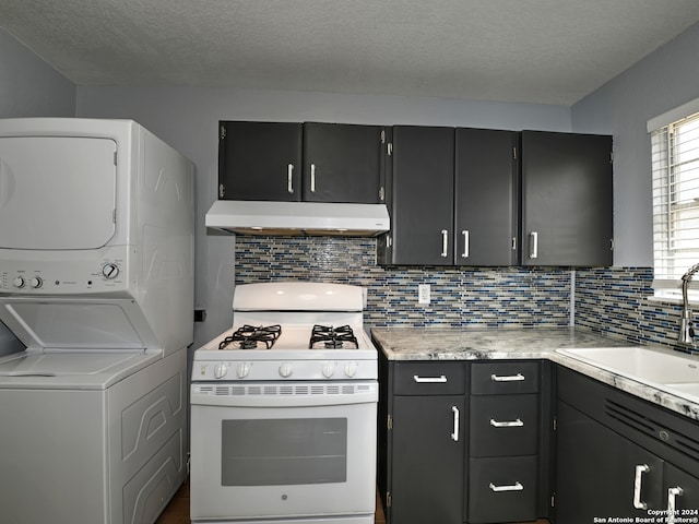 kitchen with white gas range, sink, backsplash, stacked washer and clothes dryer, and exhaust hood