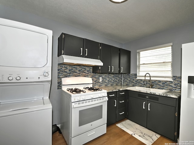 kitchen with dark wood-type flooring, stacked washer / drying machine, sink, white appliances, and backsplash