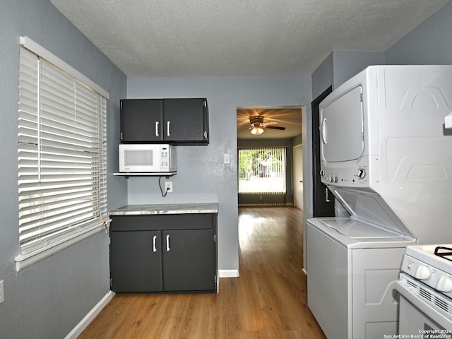 laundry area featuring ceiling fan, stacked washer and dryer, light hardwood / wood-style floors, and a textured ceiling