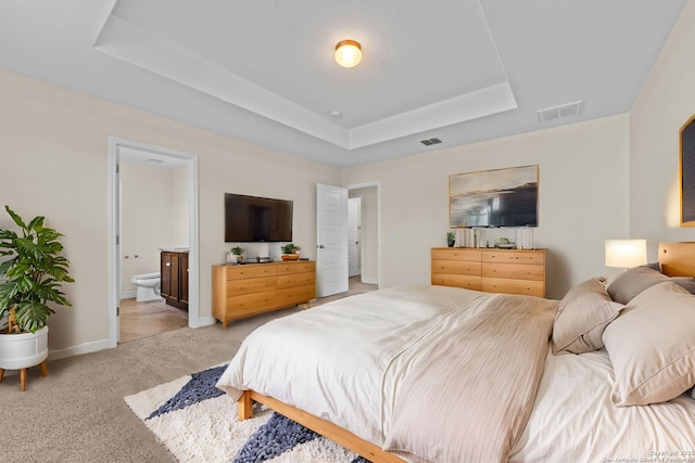 carpeted bedroom with a raised ceiling and ensuite bath