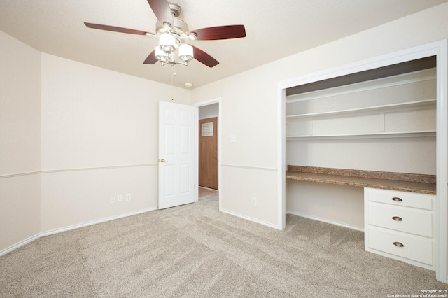 unfurnished bedroom with light carpet, built in desk, a closet, and ceiling fan