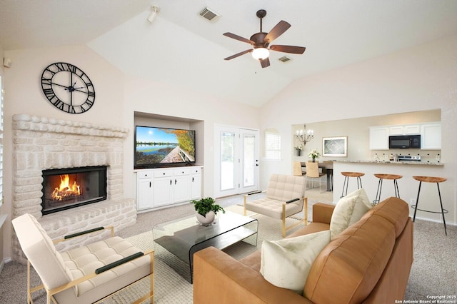 carpeted living room featuring lofted ceiling, ceiling fan with notable chandelier, and a brick fireplace