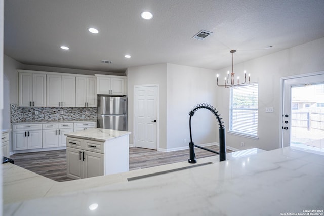 kitchen featuring decorative light fixtures, stainless steel refrigerator, a kitchen island, white cabinets, and backsplash